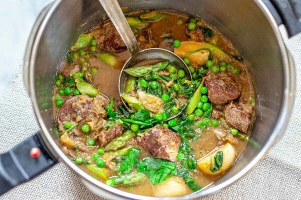 Lamb Stew Recipe - close up of pot of lamb stew with ladle and peas