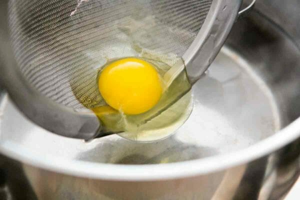 lower raw egg into simmering water to make poached egg