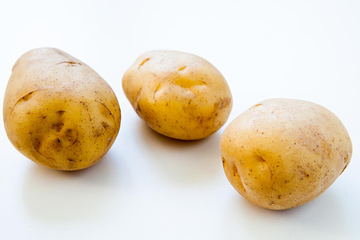 Three Yukon Gold Potatoes on White Surface