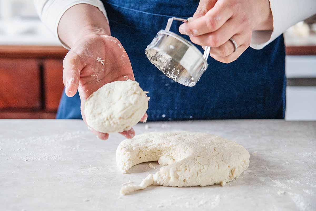 Homemade Biscuit Recipe - woman cutting biscuits out of a round of dough with a biscuit cutter