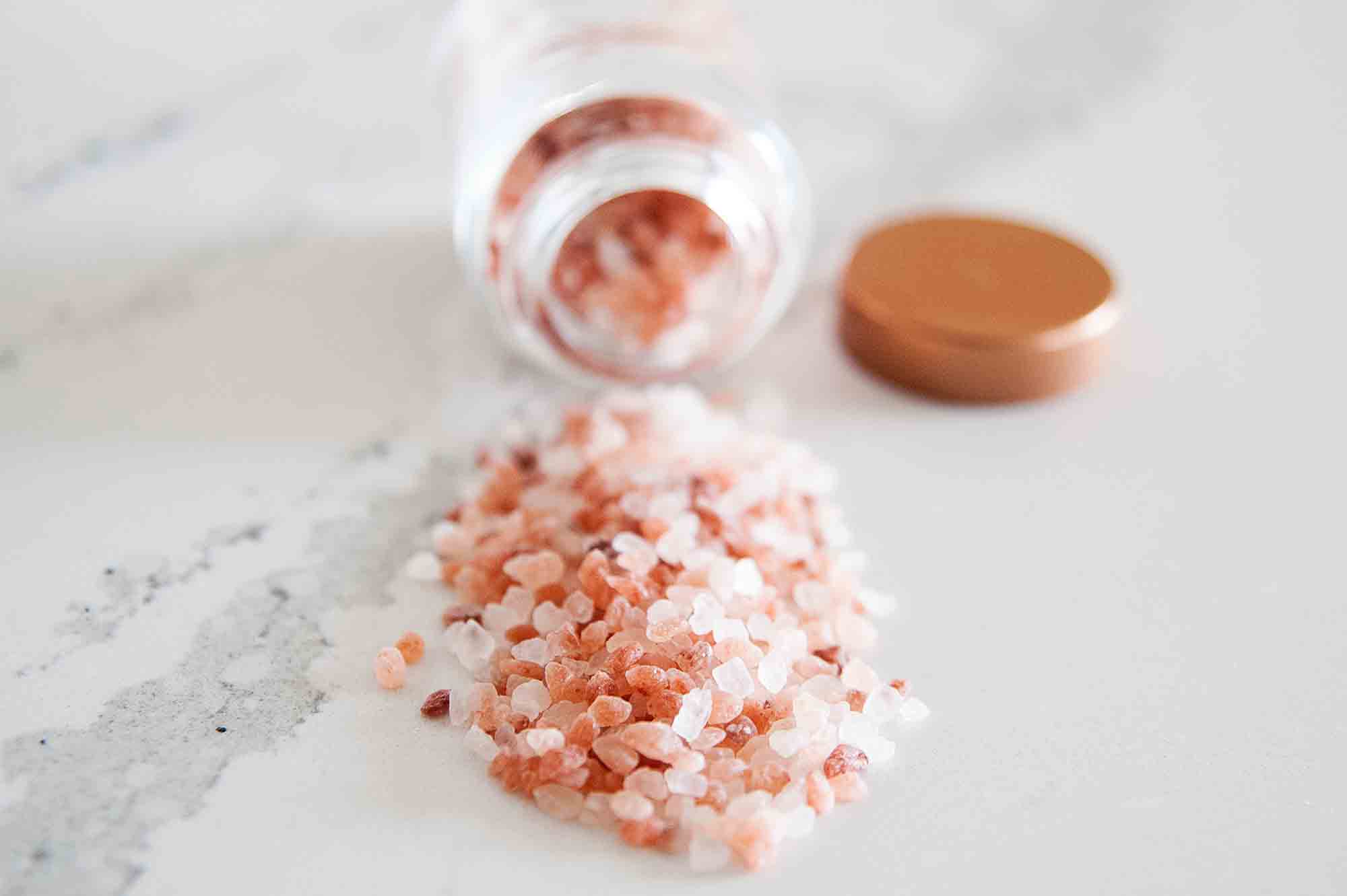 Himalayan sea salt in jar spilled on counter tip with copper lid