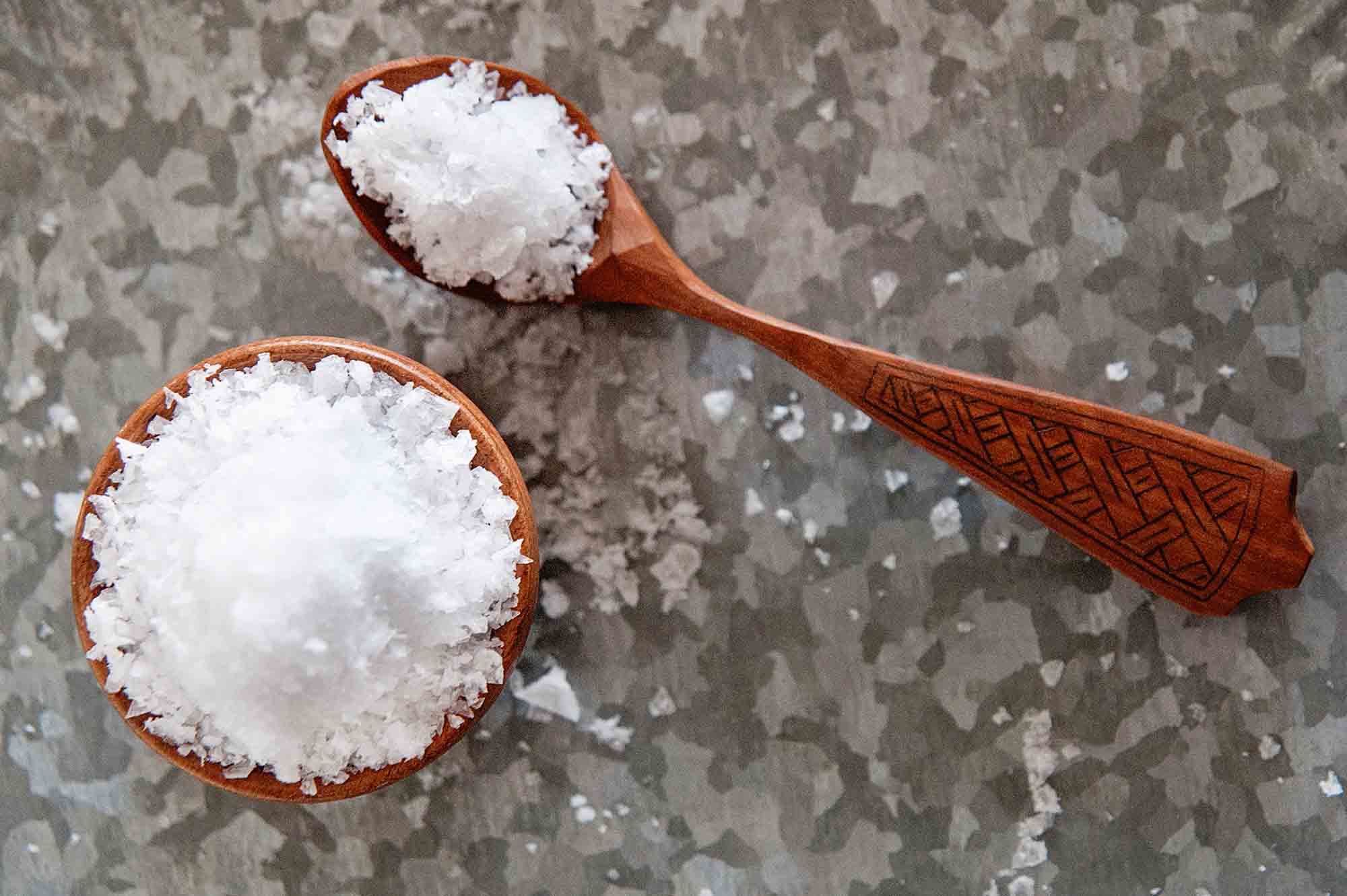 Flaky sea salt in bowl with small wooden spoon