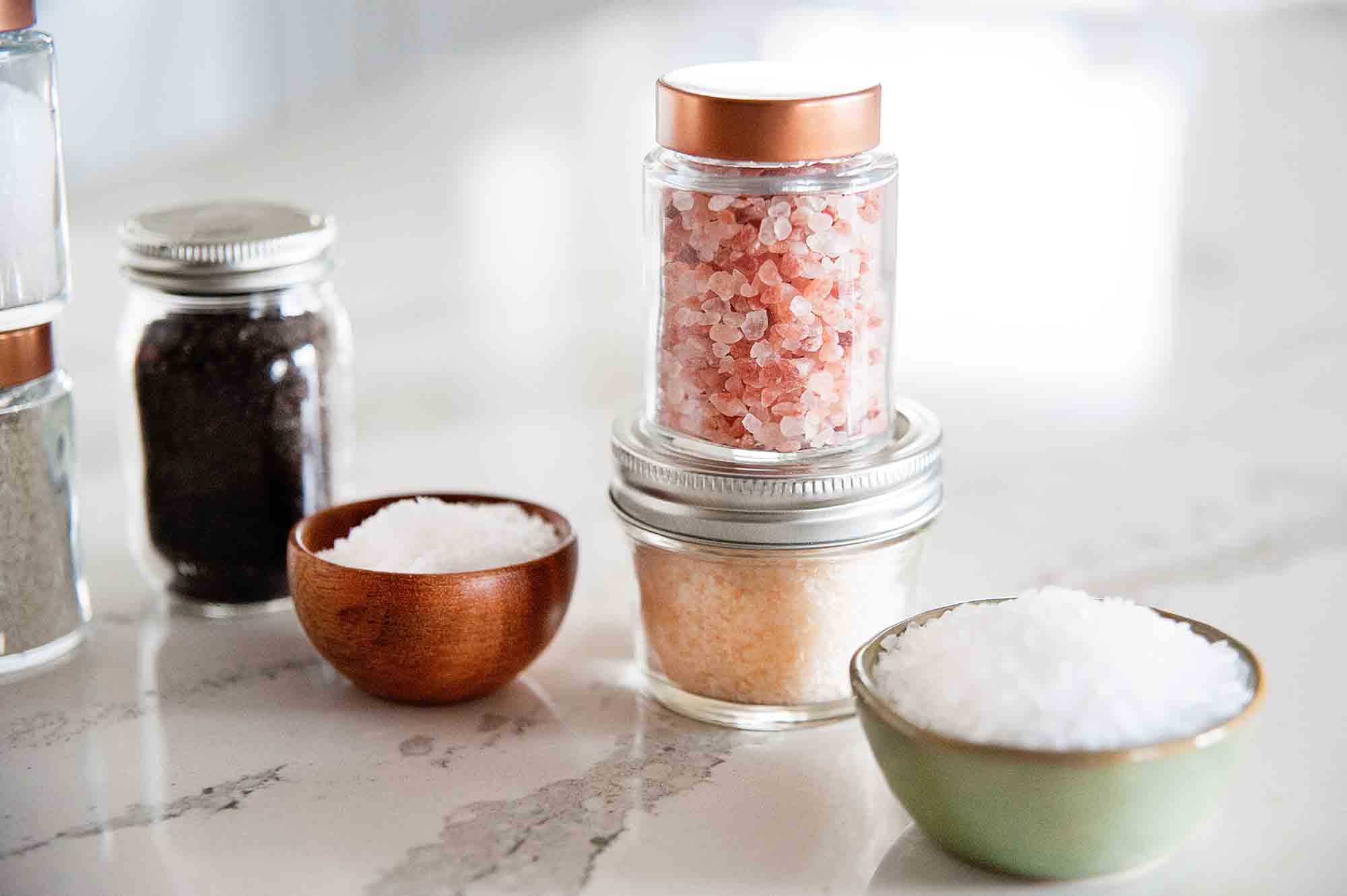 Jars and bowls of kosher salt, Himalyan salt, and smoked salt