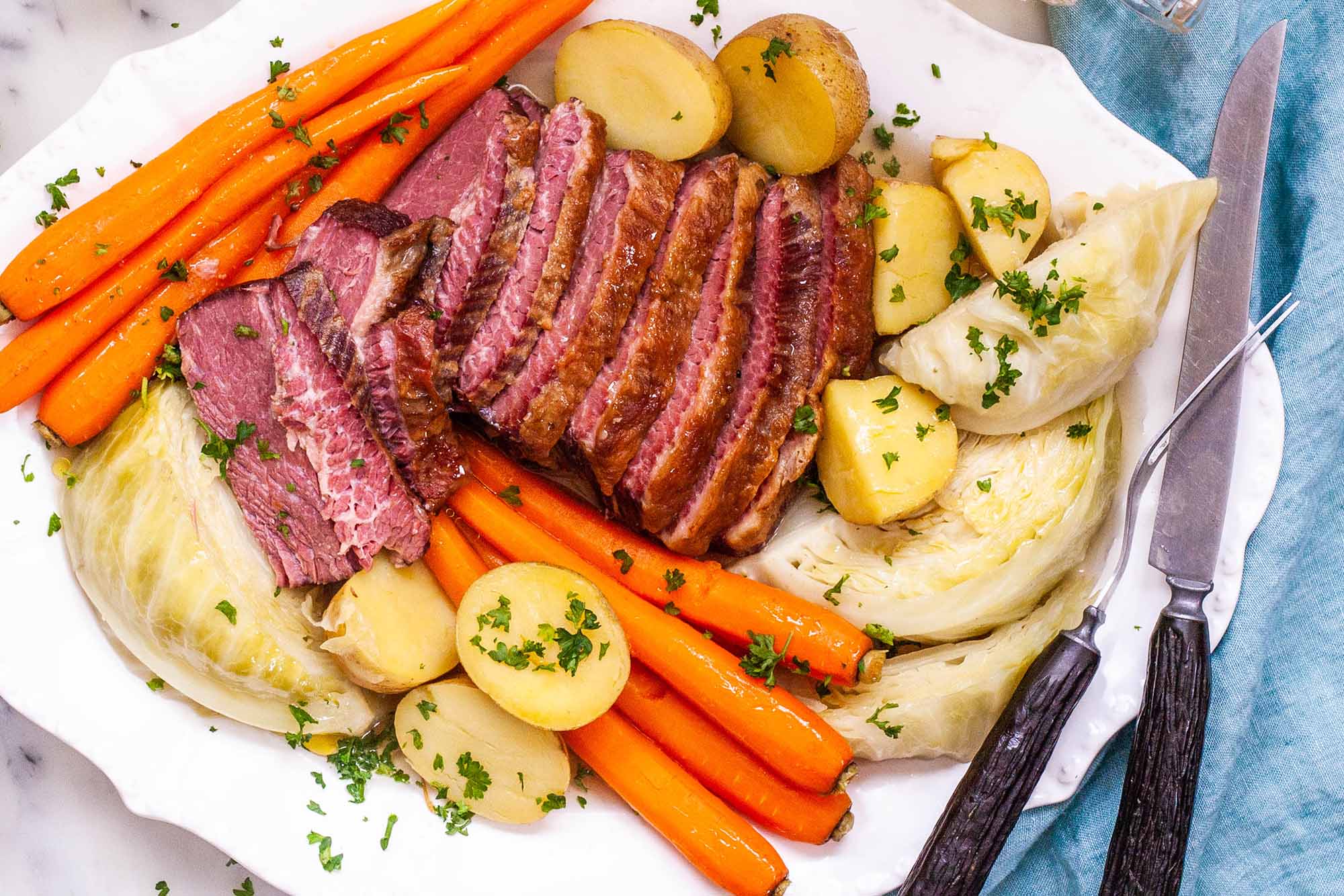 Best Boiled Corned Beef and Cabbage Recipe - platter of sliced corned beef, carrots, potatoes, and cabbage sprinkled with herbs