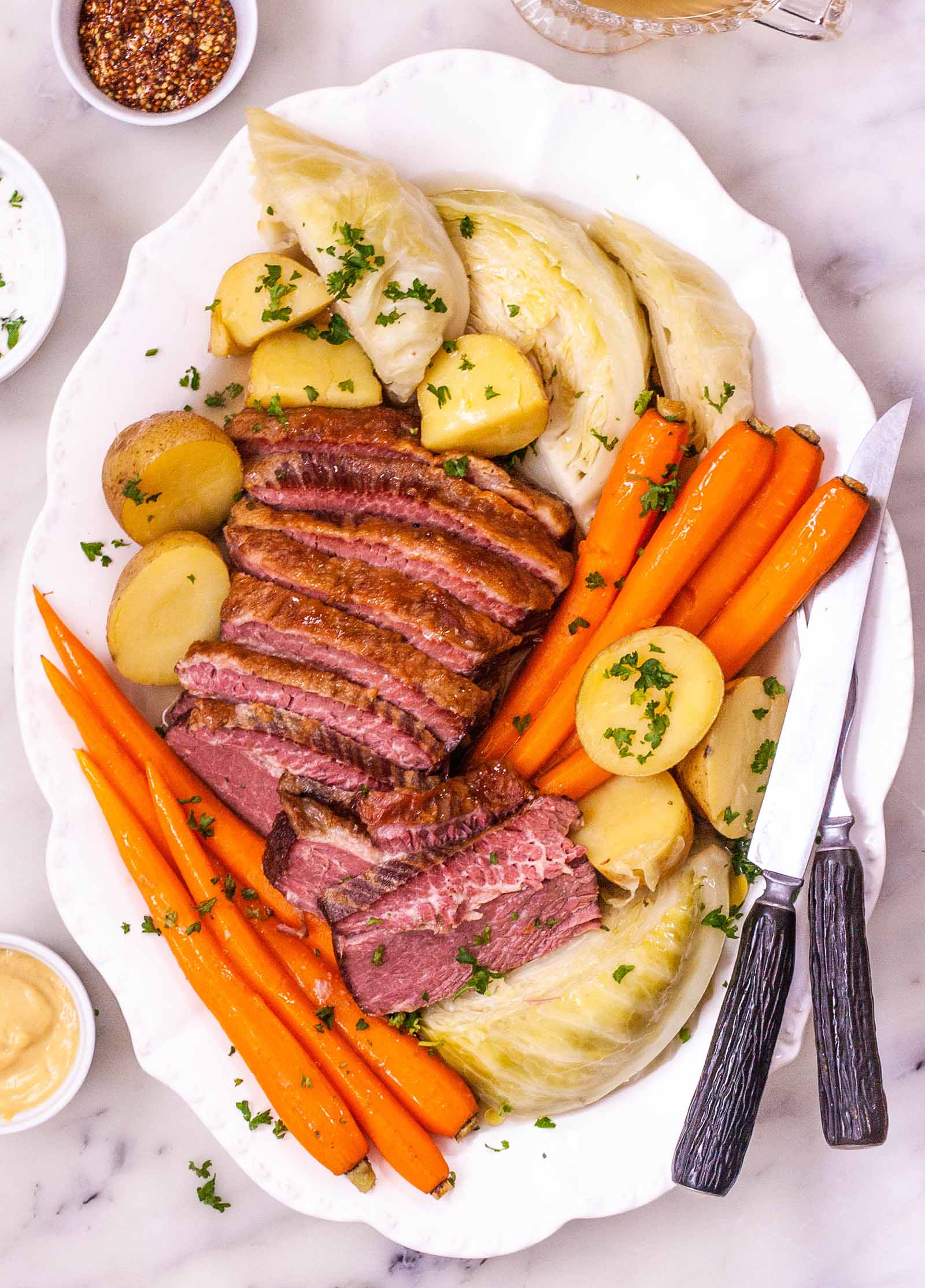 How to Boil Corned Beef and Cabbage - platter of sliced corned beef, carrots, potatoes, and cabbage sprinkled with herbs