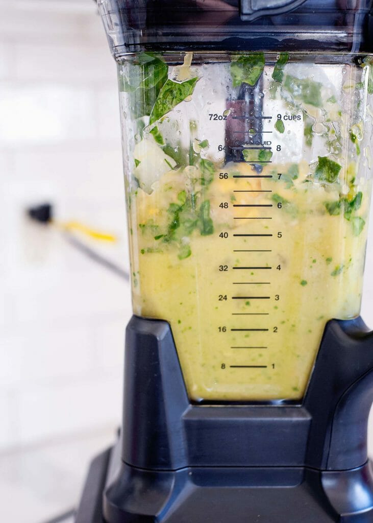 Close up view of a high speed blender jar with spinach and fruit partially processed inside.