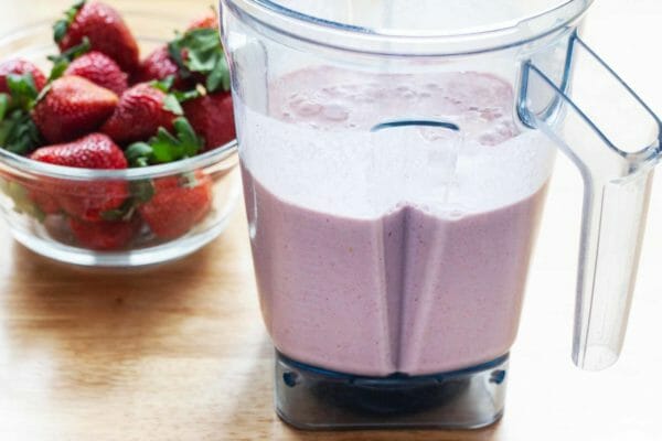 Blended breakfast smoothie in a blender with a bowl of strawberries to the left.