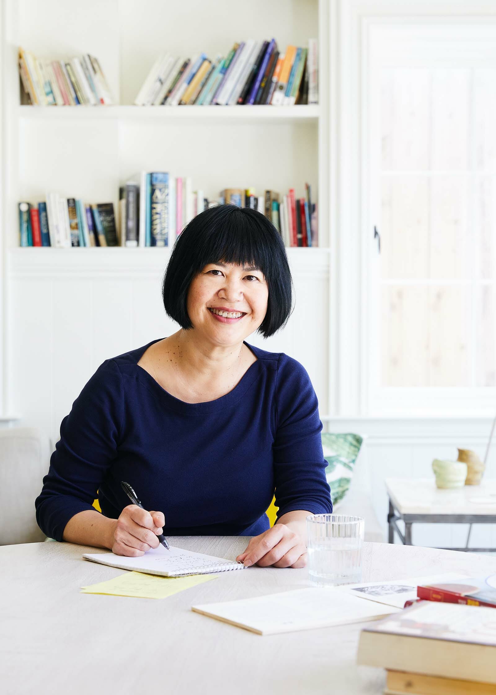 Andrea Nguyen sitting at a table smiling with a pen and paper in front of her.