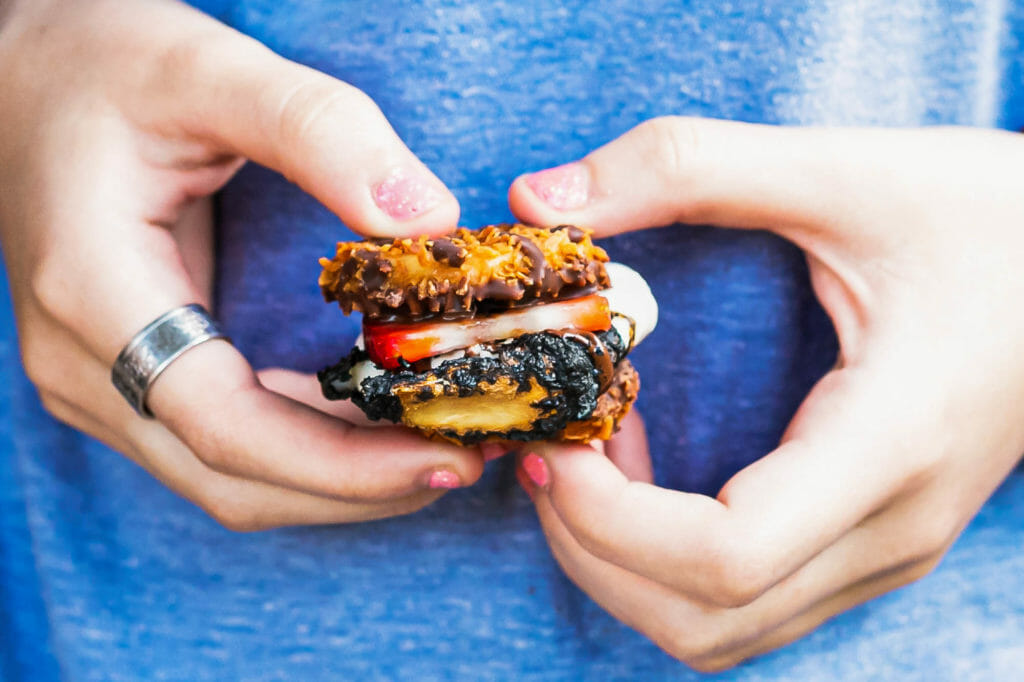 An adult holds a cookie and strawberry layered smore in a backyard smore party.