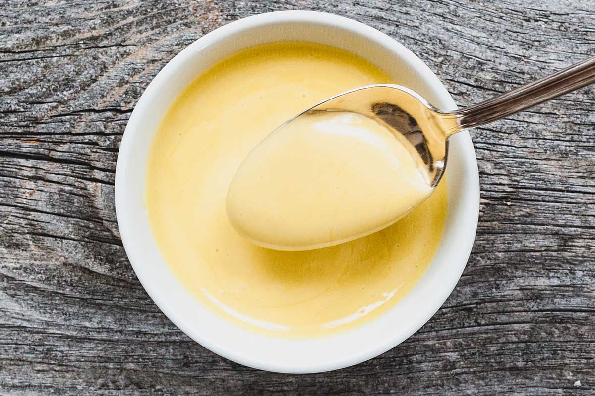 A spoonful of aioli sauce sits above a bowl with more sauce inside.