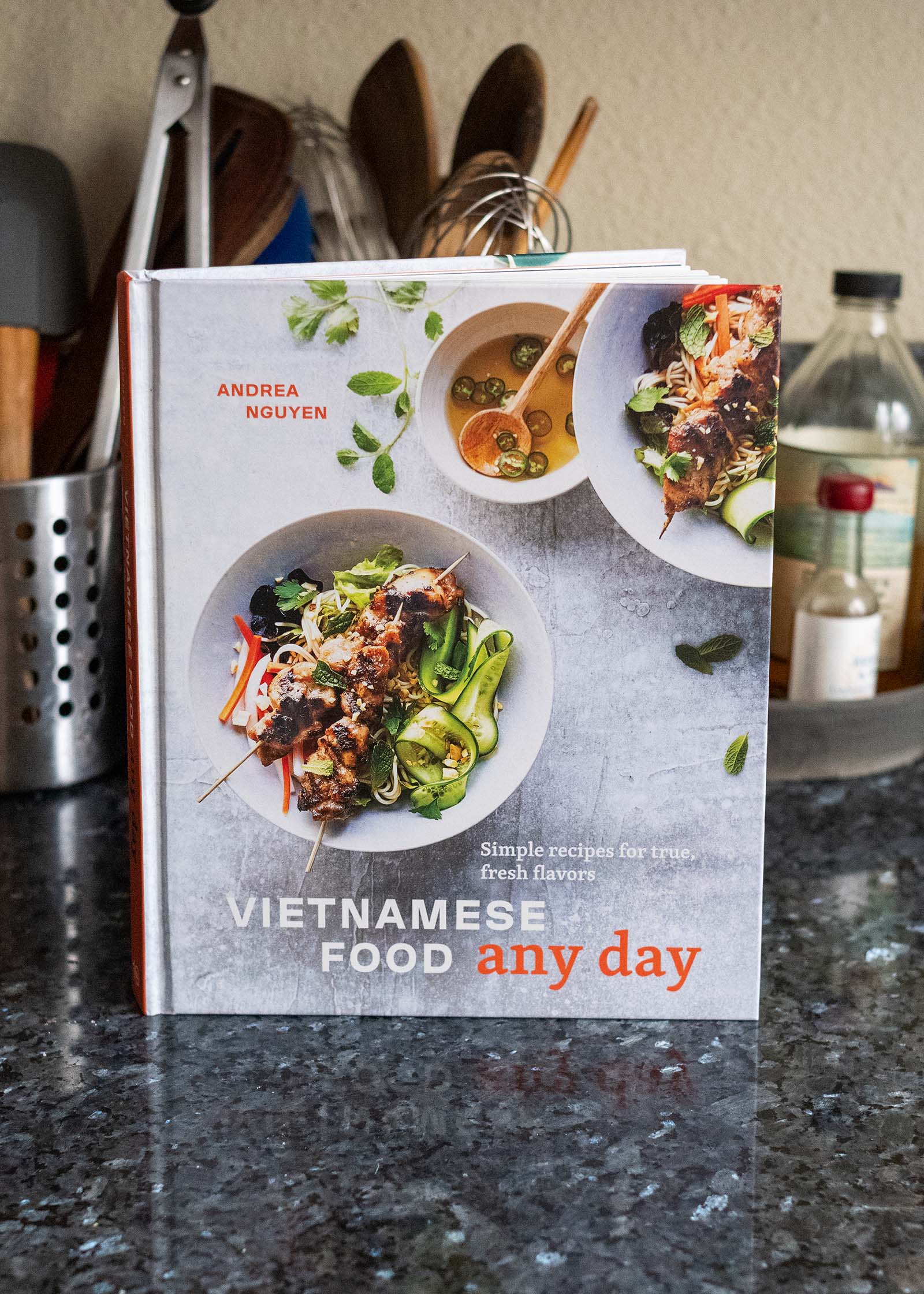 "Vietnamese Food Any Day" cookbook set on kitchen counter with utensils in the background.