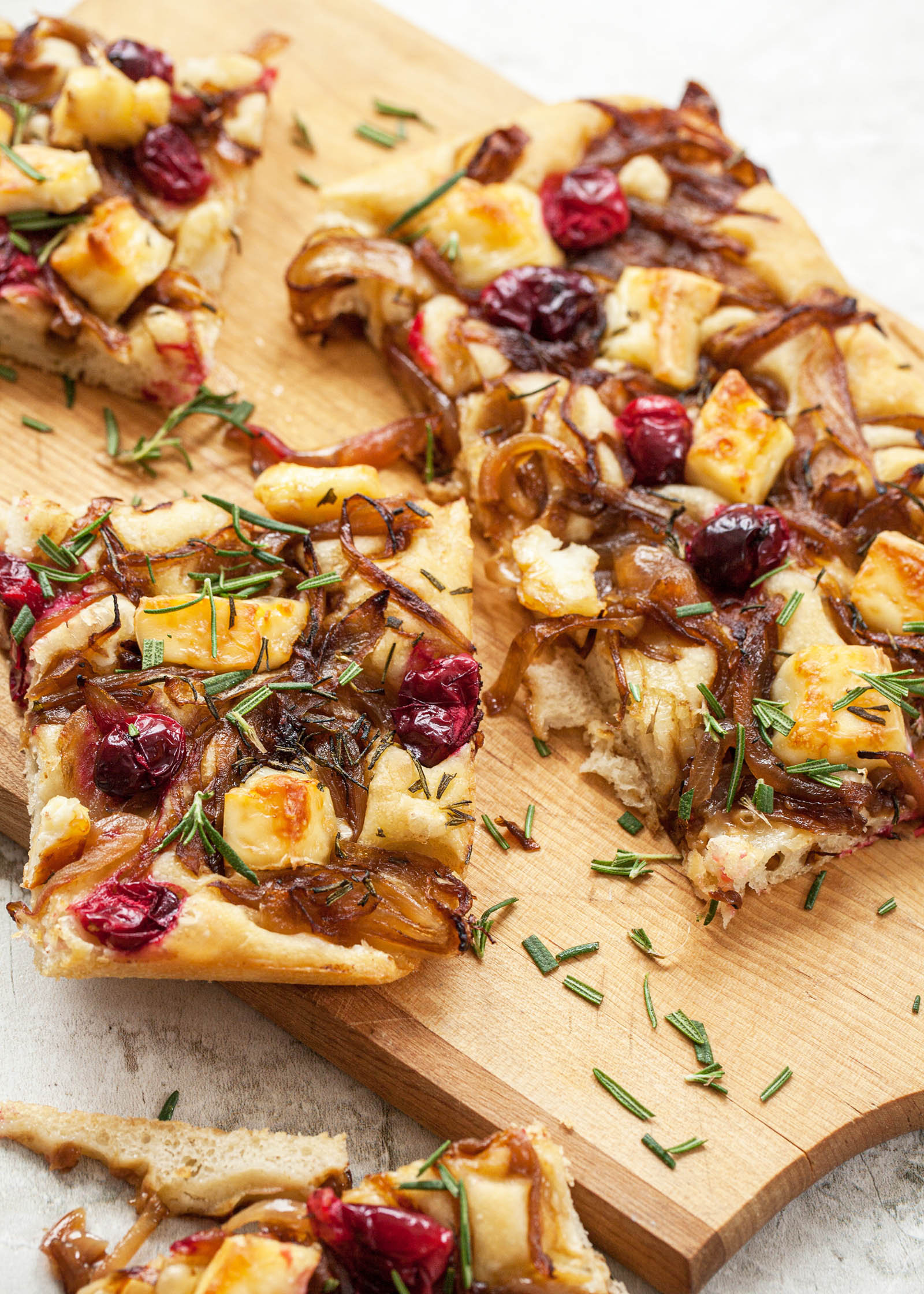 Focaccia topped with caramelized onions, cranberries, and brie and cut into slices set on a serving board.