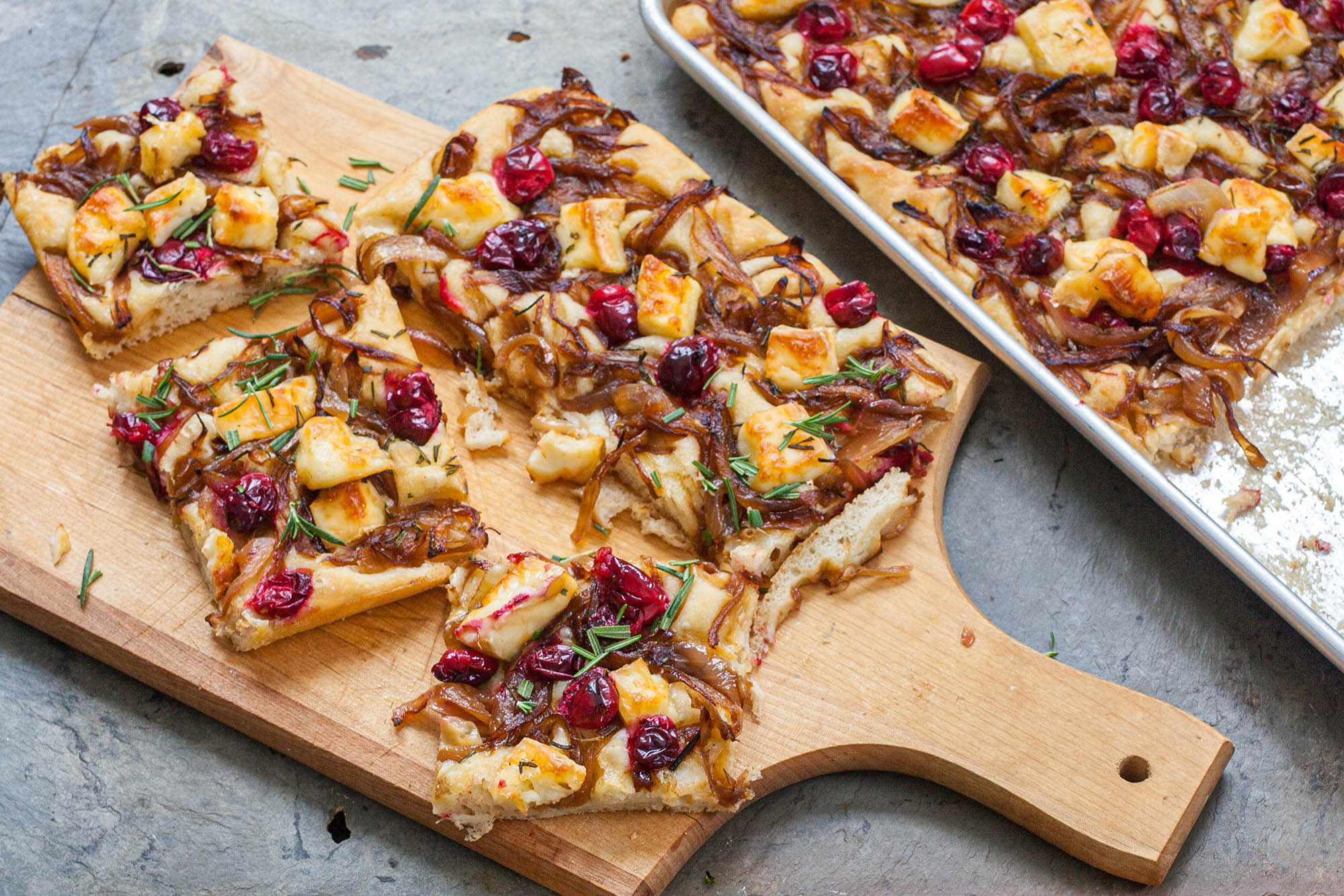 A cutting board with slices of focaccia topped with caramelized onions, cranberries, and brie.