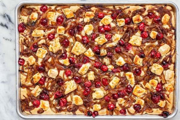 A sheet pan with foccacia topped with caramelized onion, cranberry, and brie.