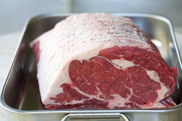 Uncooked prime rib sprinkled with salt and pepper in a roasting pan