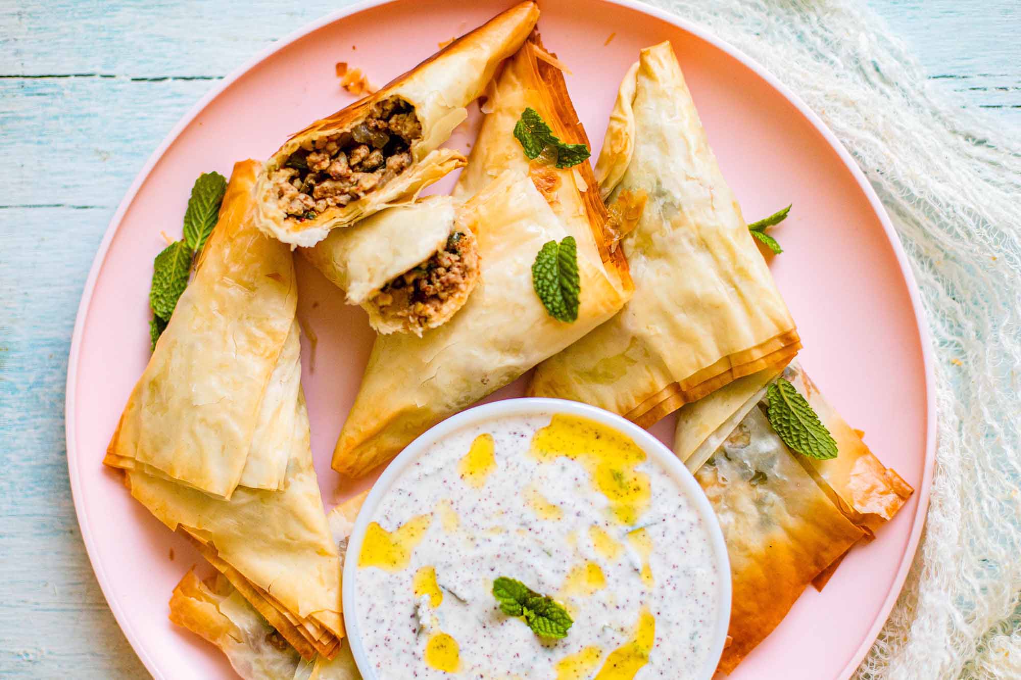 Easy Baked Indian Chicken Tikki Masala Samosa folded into a triangle with Mint Yogurt Dip on a pink plate with one samosa broken open.