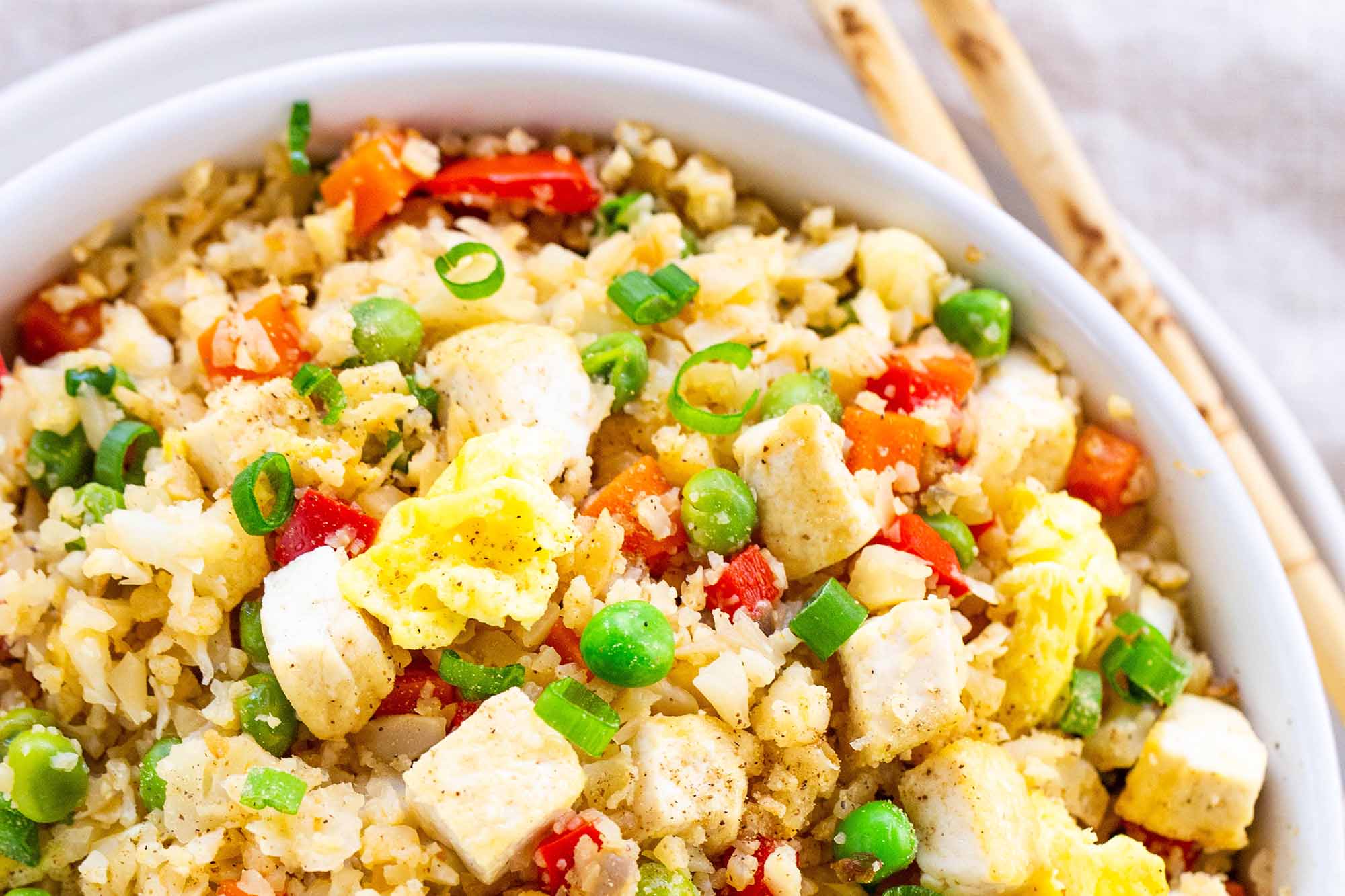Vegan Cauliflower Fried Rice -- bowl of low carb fried rice with peas, eggs, and tofu