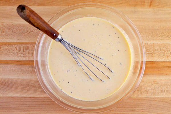 A whisk and glass bowl filled with the egg mixture to make an Easy Breakfast Casserole with Mushrooms, Brussels Sprouts, and Goat Cheese.