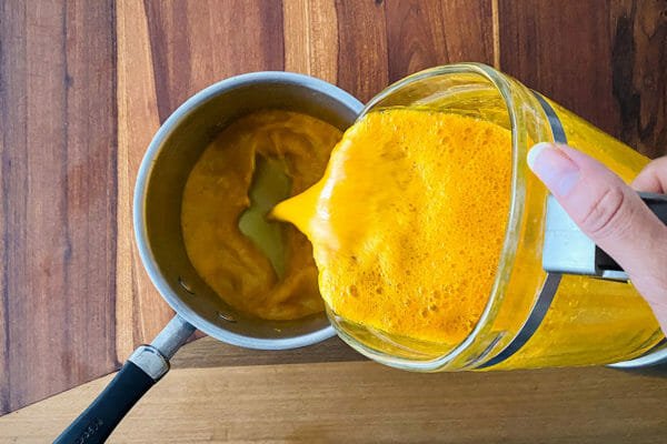 Pouring a bright yellow turmeric liquid into a pot to show how to make Jamu.