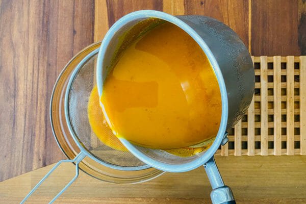 Pouring turmeric and ginger mixture through a strainer to make homemade Jamu.
