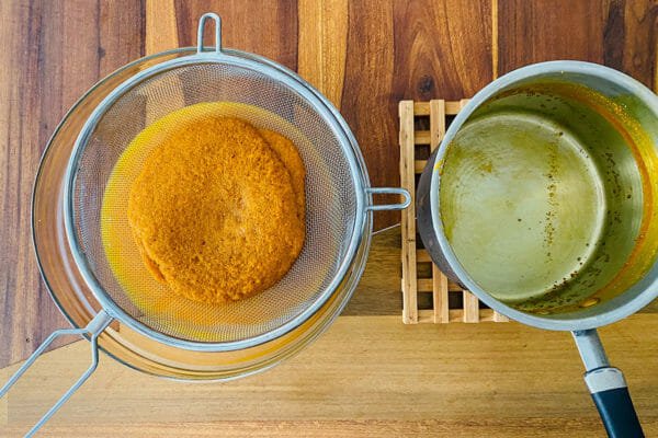 Ground turmeric in a strainer with a pot set next to it to make a Tumeric and Ginger Elixir.
