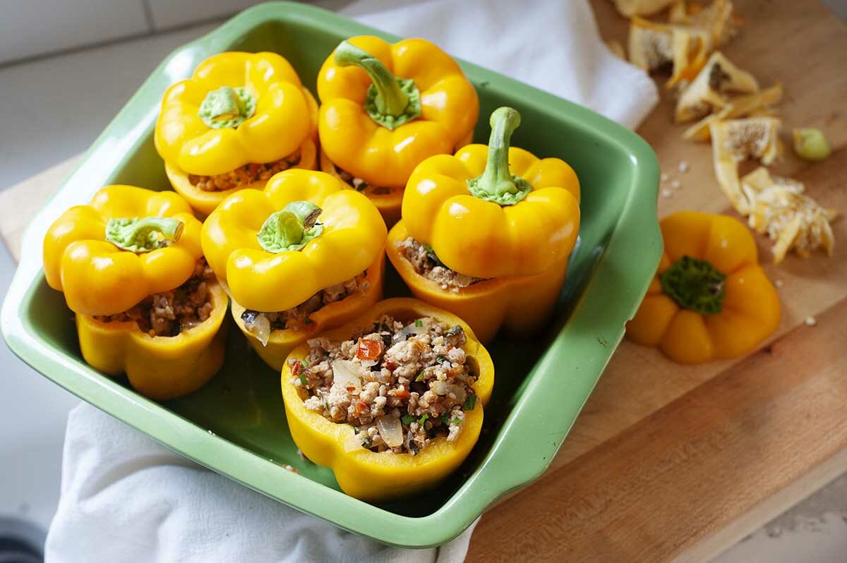 A casserole dish with five of the best stuffed peppers inside. The yellow peppers have the tops sliced off and the stuffing is visible underneath it.