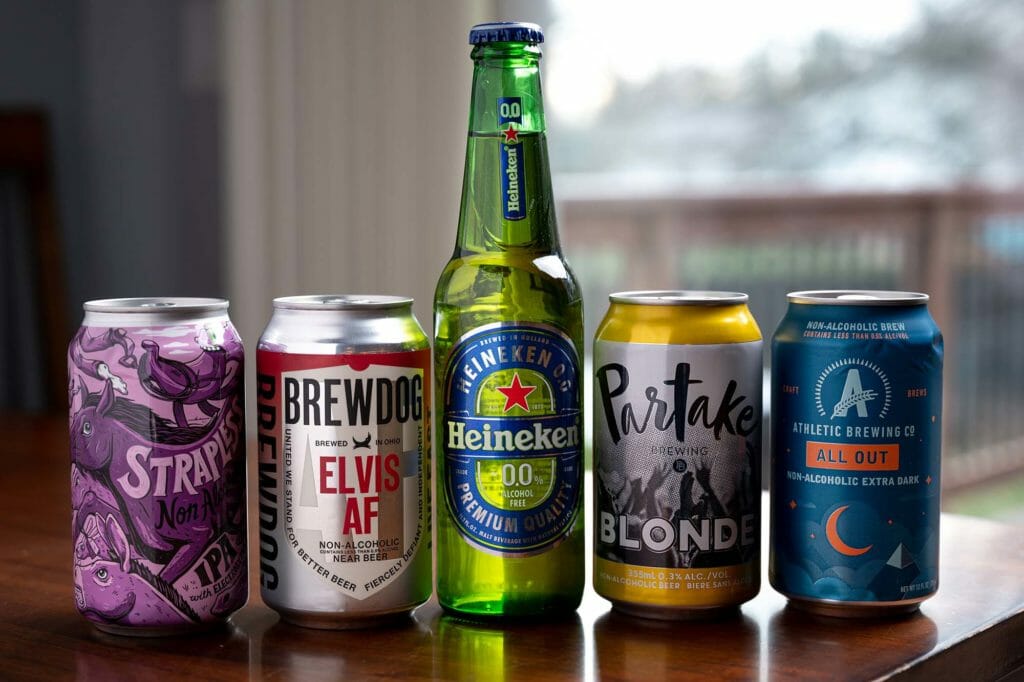 Four cans and one bottle of non-alcoholic beers are lined up on a table.