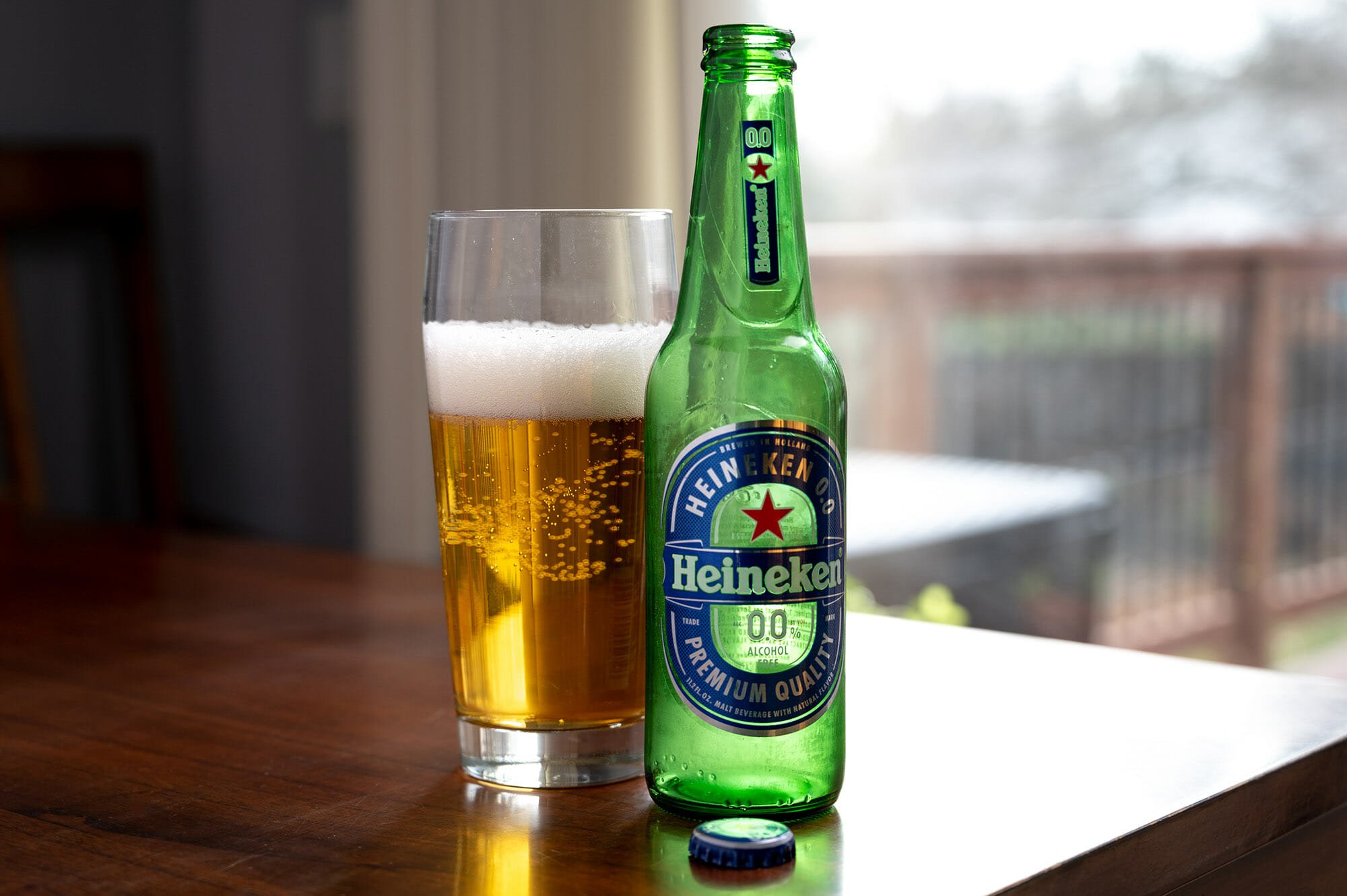 A bottle of non alcoholic beer next to a glass of Heineken.