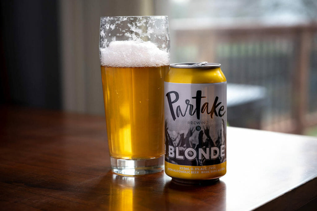 A can of non-alcoholic beer next to a glass of a light pilsner-style beer.