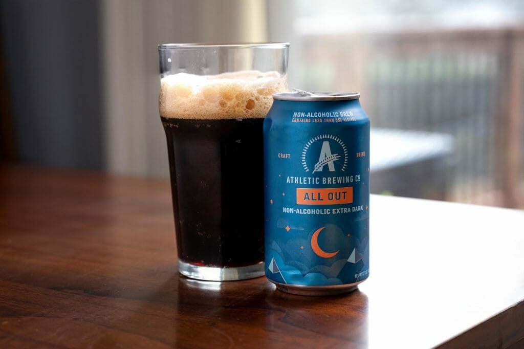 A can of non-alcoholic beer next to a glass of stout beer.