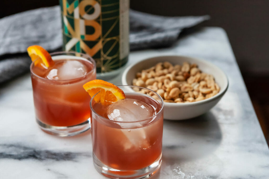 Two alcohol free negronis in rocks glasses with an orange wedge and bar nuts.