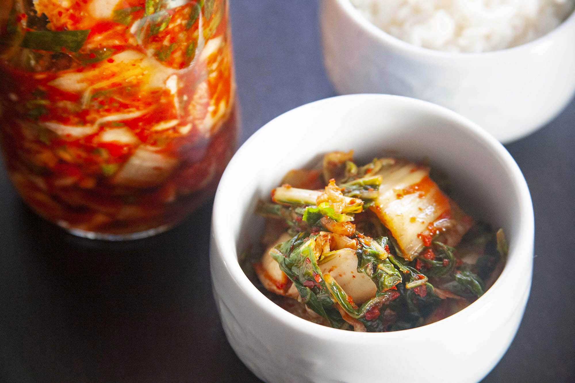 A bowl with easy homemade kimchi is in front of the jar of it and white rice is behind it.